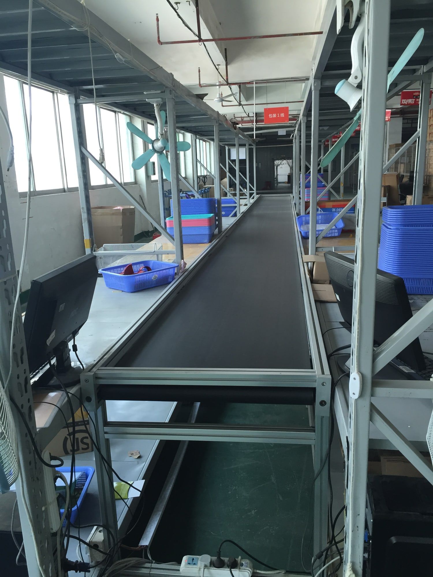A conveyor belt runs between workstations and stacks of blue crates.